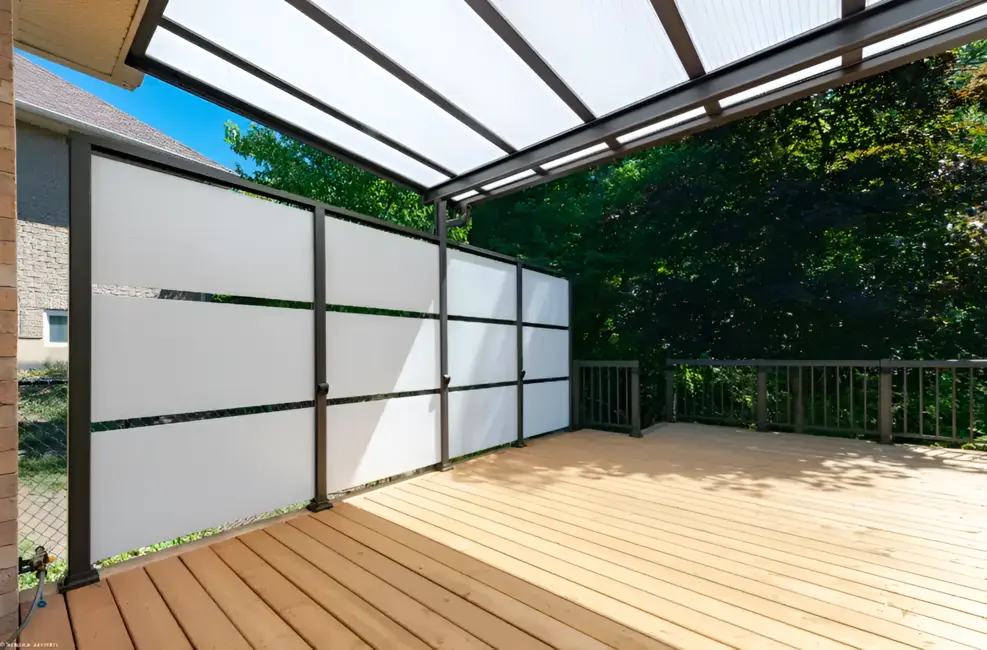 A white privacy wall with a black aluminum frame installed on a wooden residential deck next to an outdoor grill.