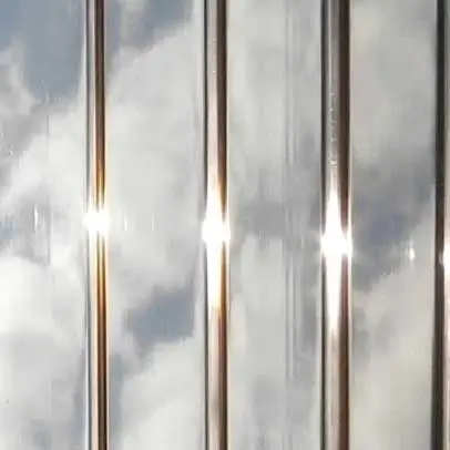 Close-up of ribbed, bronze-tinted translucent sunroom roofing material reflecting a cloudy blue sky.
